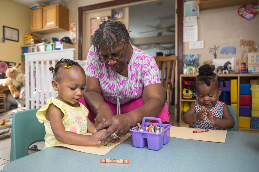 Teacher helping girl draw with crayons