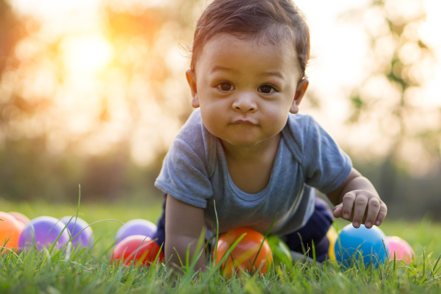 Young boy crawling in grass with balls around him