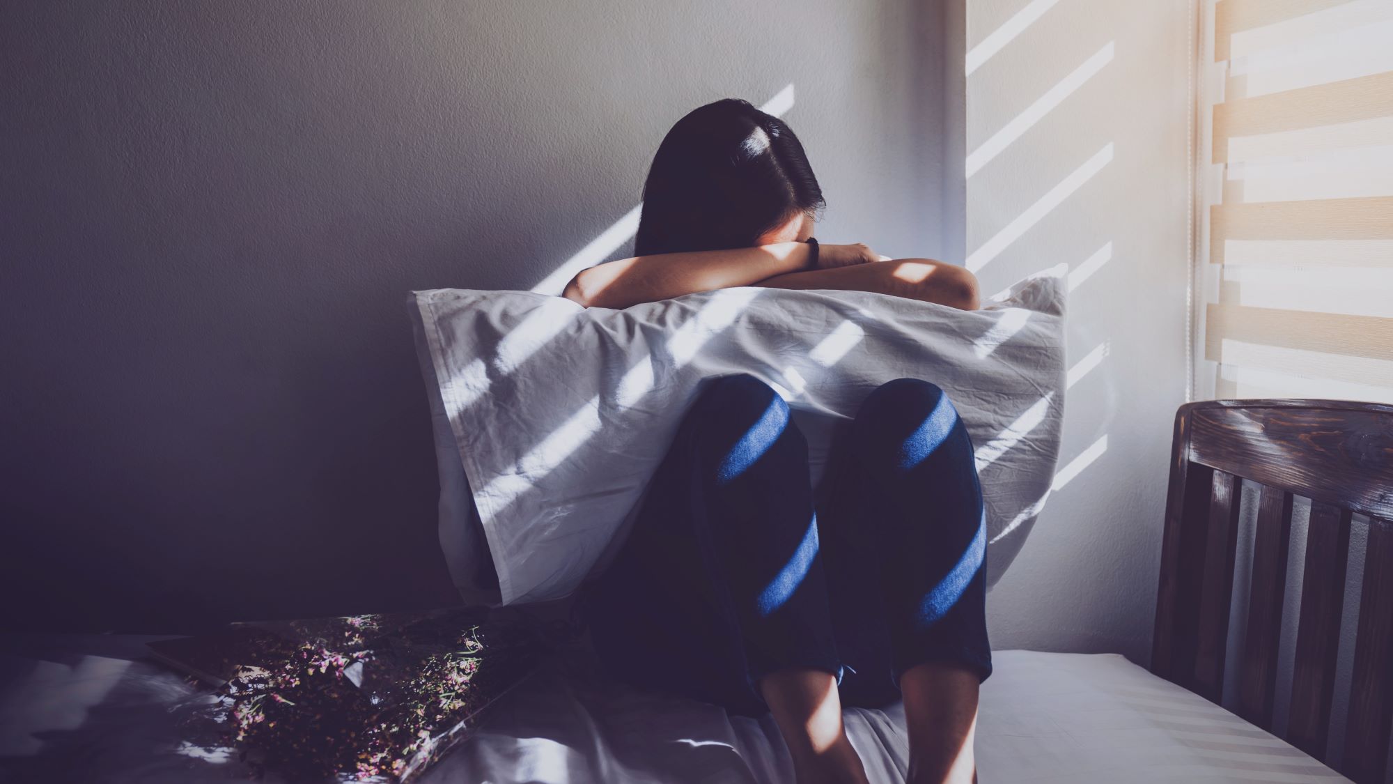 Teen girl on a bed, burying her head in a pillow in a dark room.
