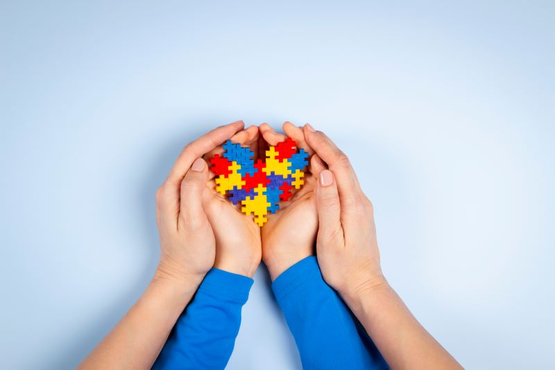 A child's hands holding a puzzle shaped like a heart with the parent's hands surrounding the child's.
