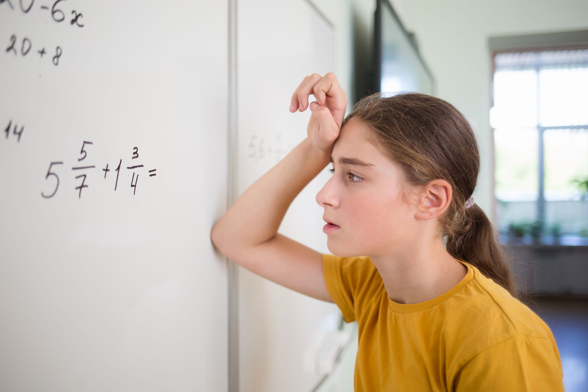 A teenage girl leans against a white board while struggling to figure out a formula on the board.