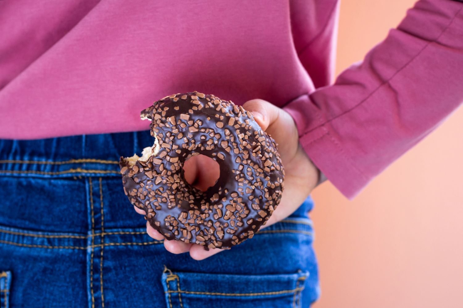 A little girl in a pink top hiding a donut behind her back.