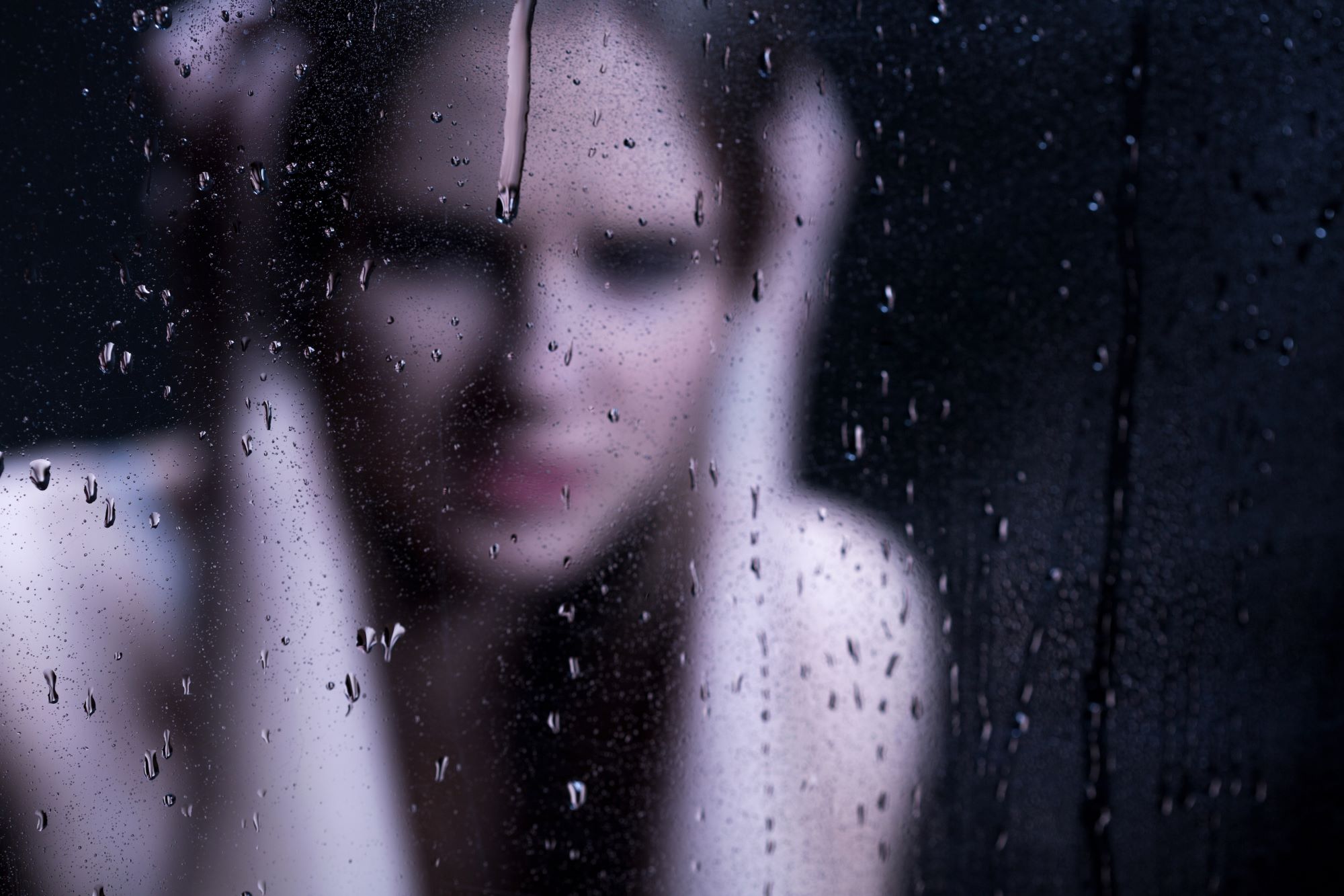 A depressed teen covering her ears, blurry behind a rainy pane of glass.
