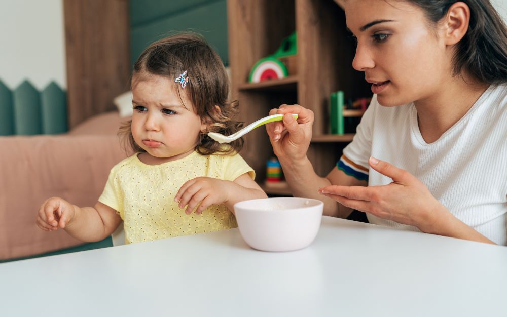 A grumpy little girl refusing to eat what her mother is offering her on a spoon.