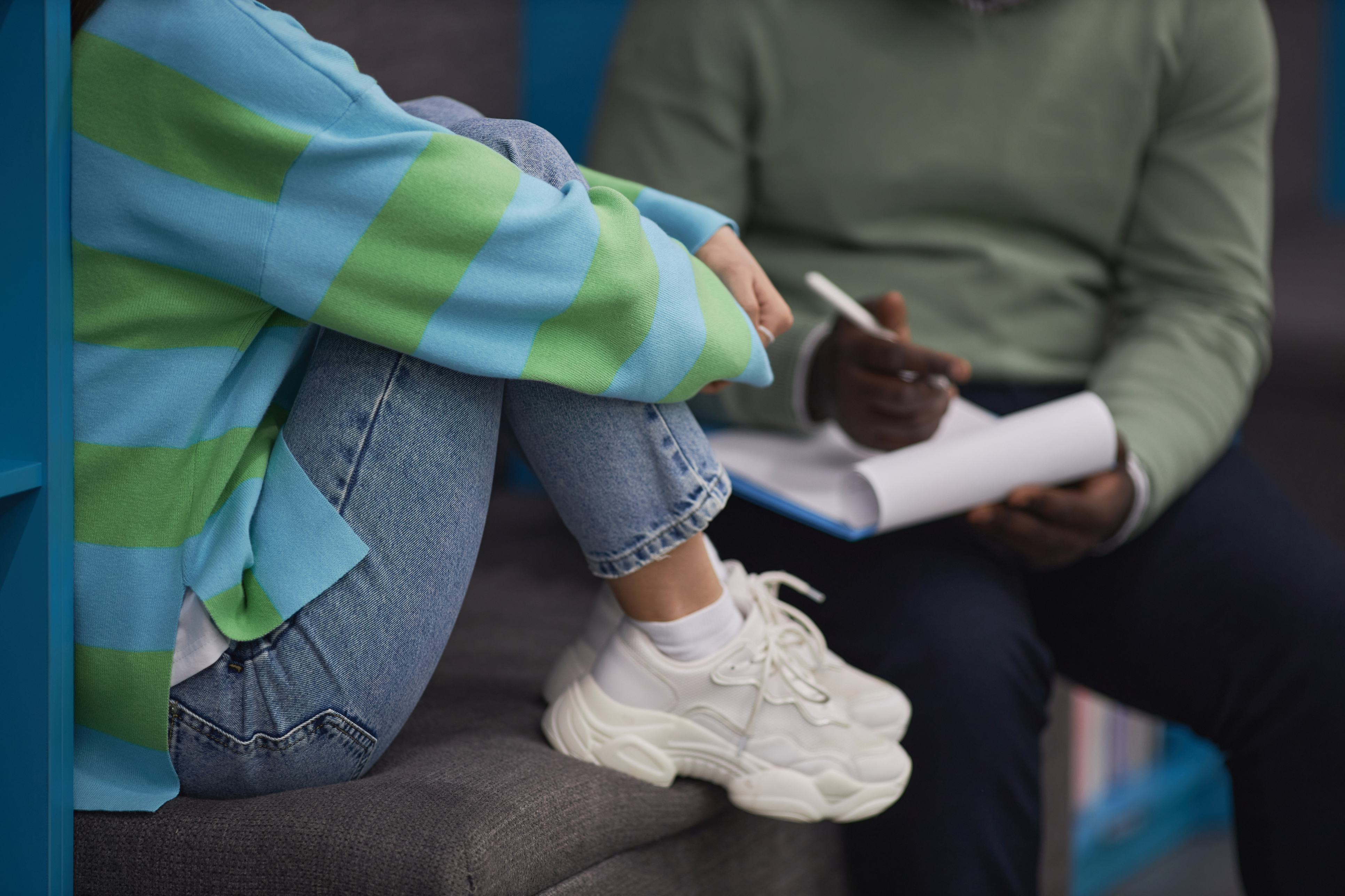 A teenage girl hugging her knees talking to a therapist.