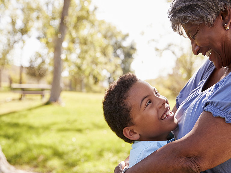 Smiling little boy hugging his grandmother at the park.