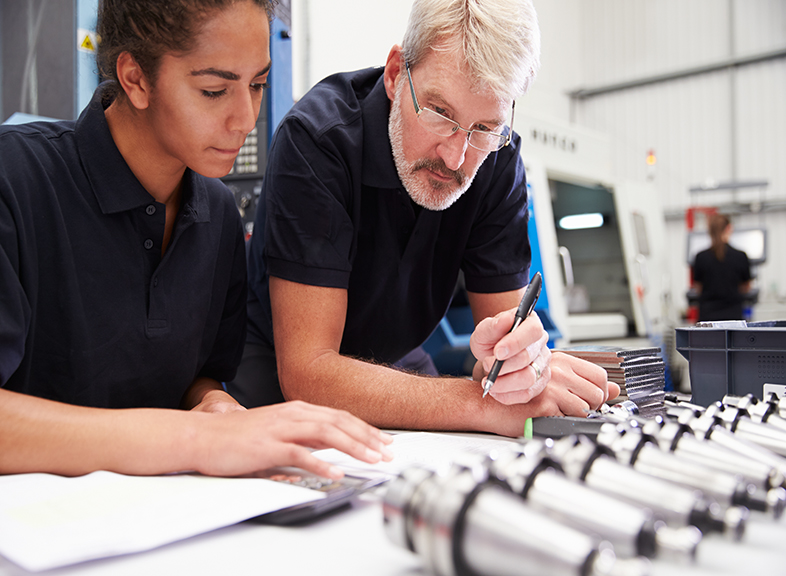 Teen works with a mentor on engineering equipment.