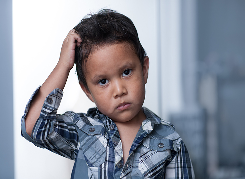 Sad little boy pulling at his short dark hair.