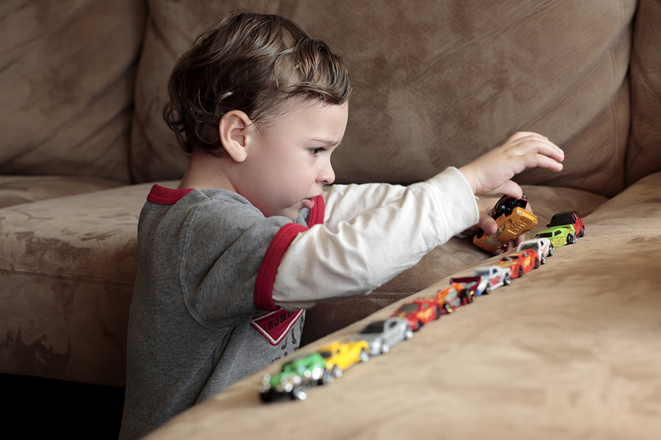 Little boy lining up painted toy cars on a brown couch.