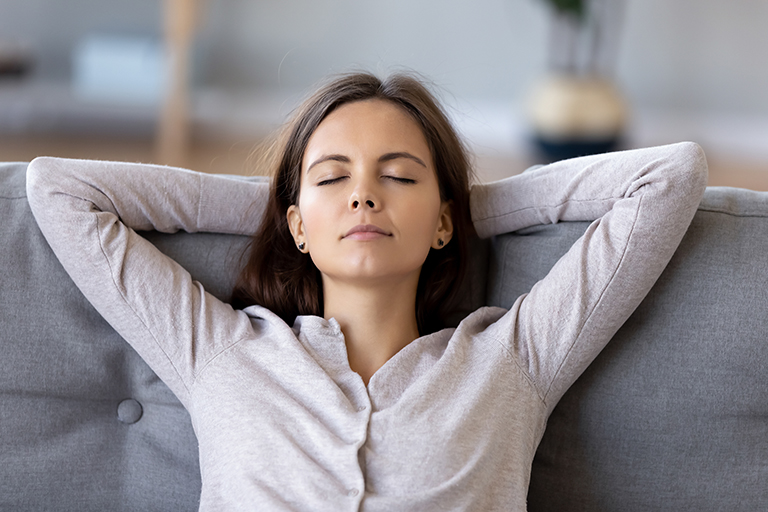 Mother with eyes closed and hands behind her head resting on a couch.