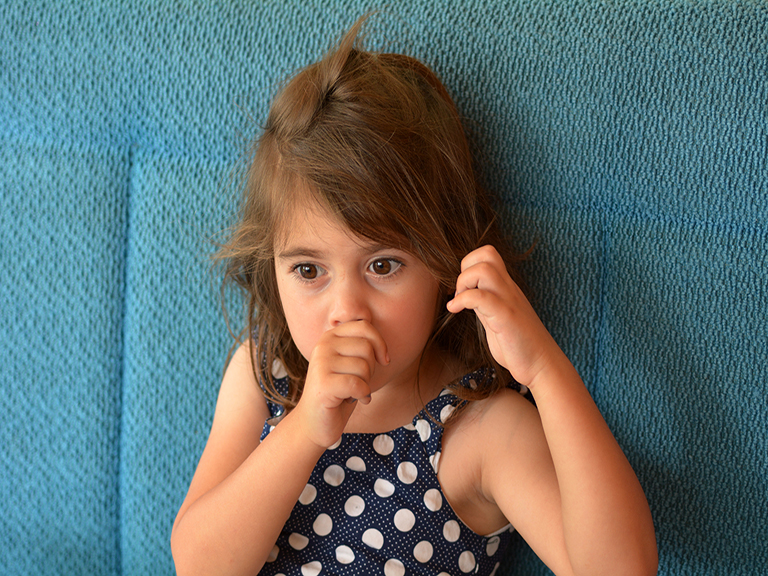 Little girl, looking concerned, sitting on a couch sucking her thumb.