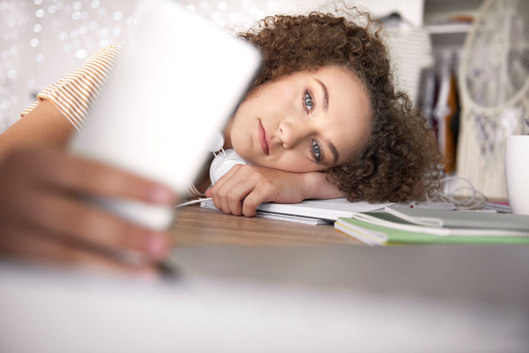 Teen girl with a sad expression lays her head on a desk and takes a selfie.
