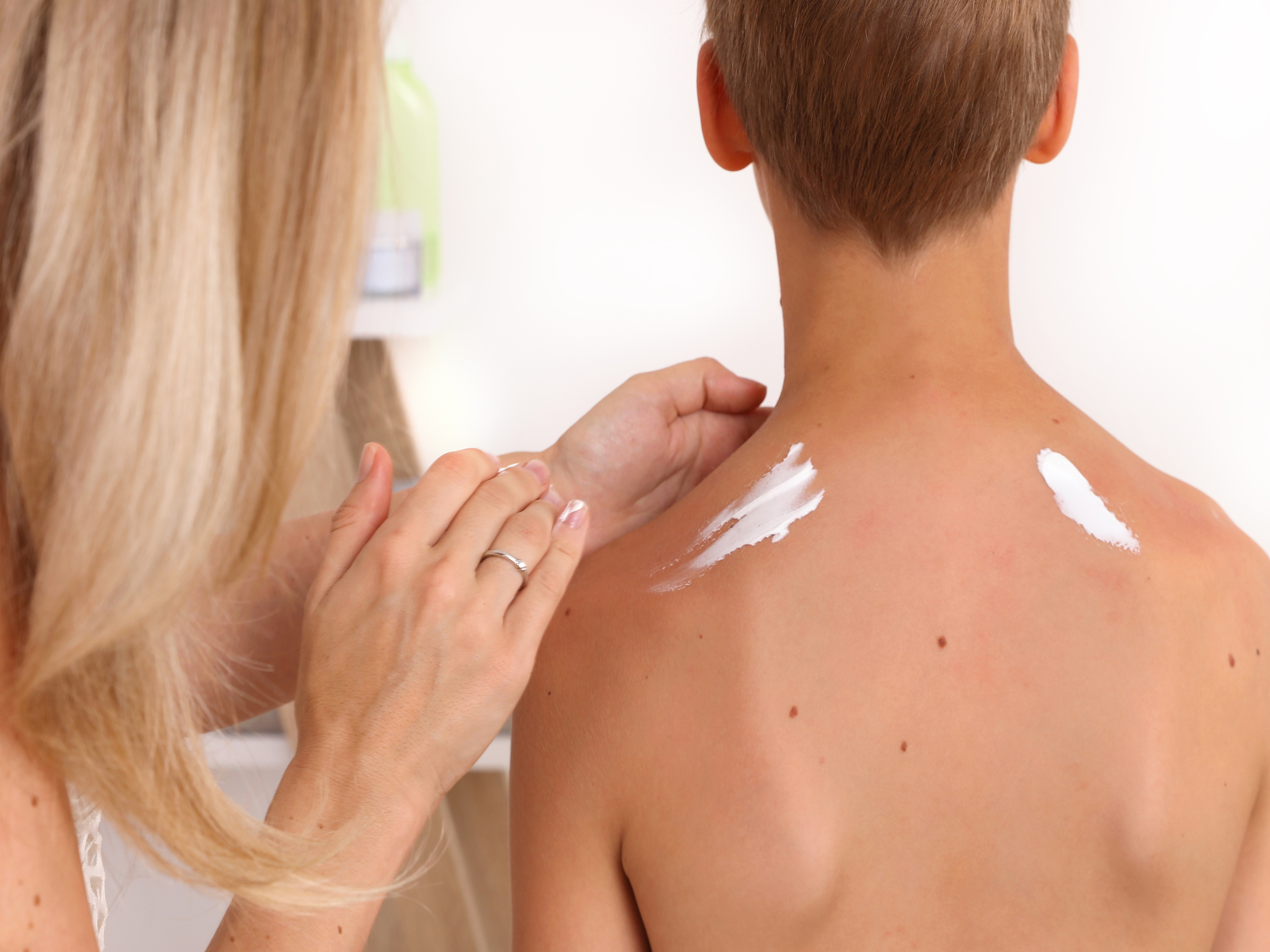 Mom applying sunscreen to son's back.