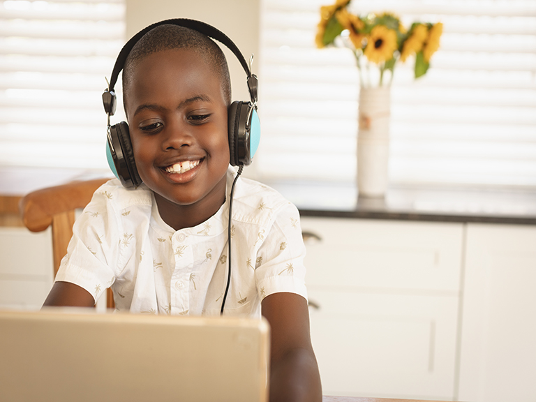 Boy smiling, with headphones in front of computer