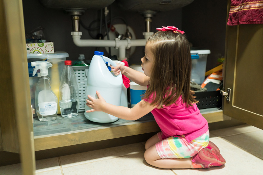 Child reaching for cleaning supplies in under sink cabinet.