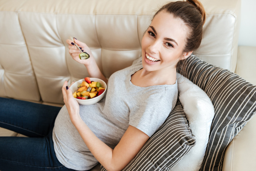 Pregnant mother eating a bowl of fruit.