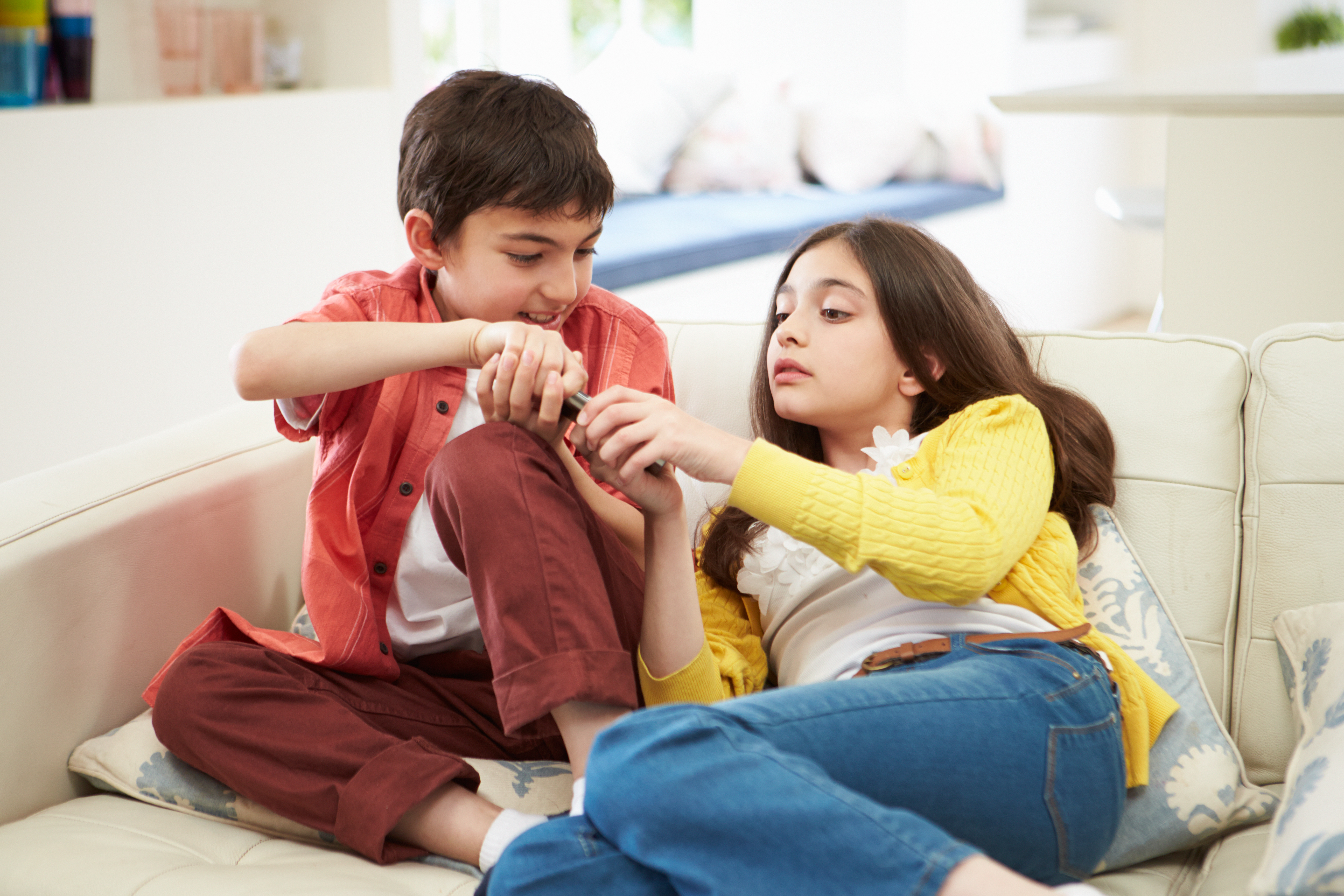 Brother and sister on a couch fighting over a remote control